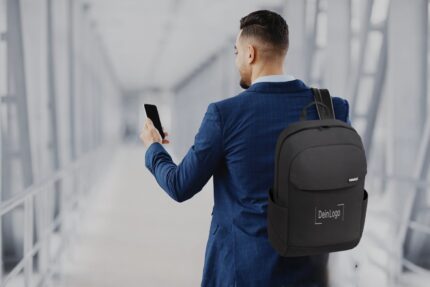 Mann in Anzug mit schwarzem Rucksack, auf dem "DeinLogo" steht, schaut auf sein Smartphone in einer modernen Umgebung.